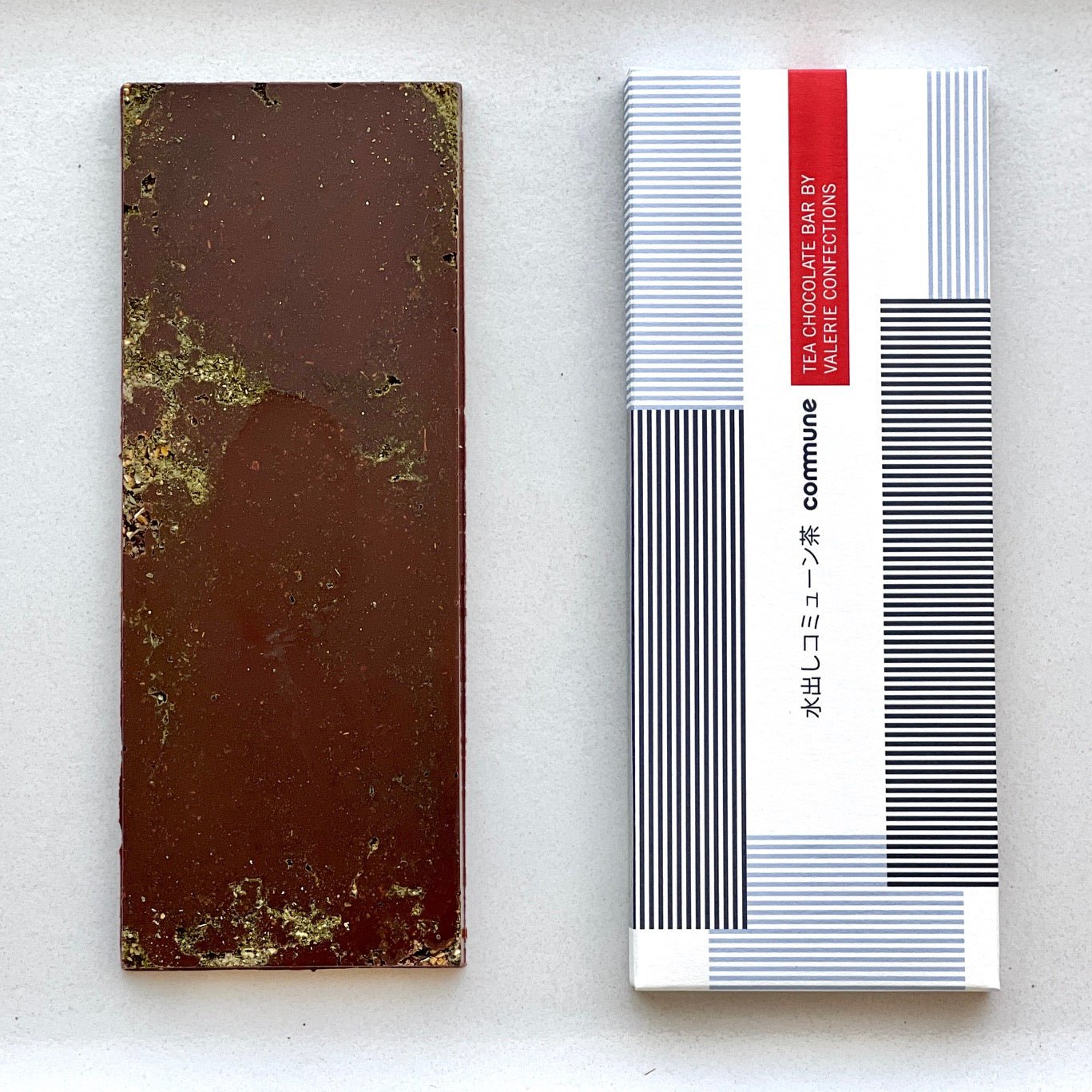 An unwrapped Commune Tea Bar revealing its rich 61% bittersweet chocolate with subtle herbal infusions, placed next to its modern, minimalist packaging.