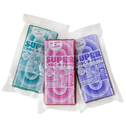Three vacuum-sealed chocolate bars in green, pink, and purple packaging with white text.
