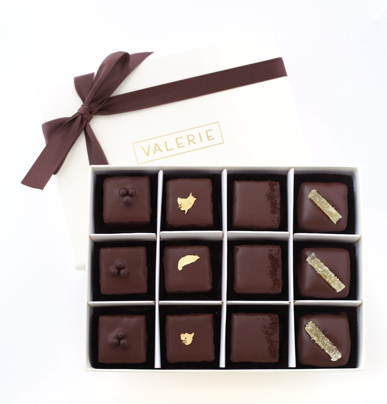 A luxurious box of Valerie Confections Bittersweet Chocolate Petits Fours, featuring an assortment of Ginger, Chocolate, Champagne, and Espresso flavors, elegantly tied with a brown satin ribbon.