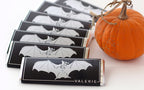 A stack of Bat Bars in black and silver wrappers, arranged next to a rustic pumpkin for a festive seasonal display.
