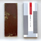 An unwrapped Commune Tea Bar revealing its rich 61% bittersweet chocolate with subtle herbal infusions, placed next to its modern, minimalist packaging.