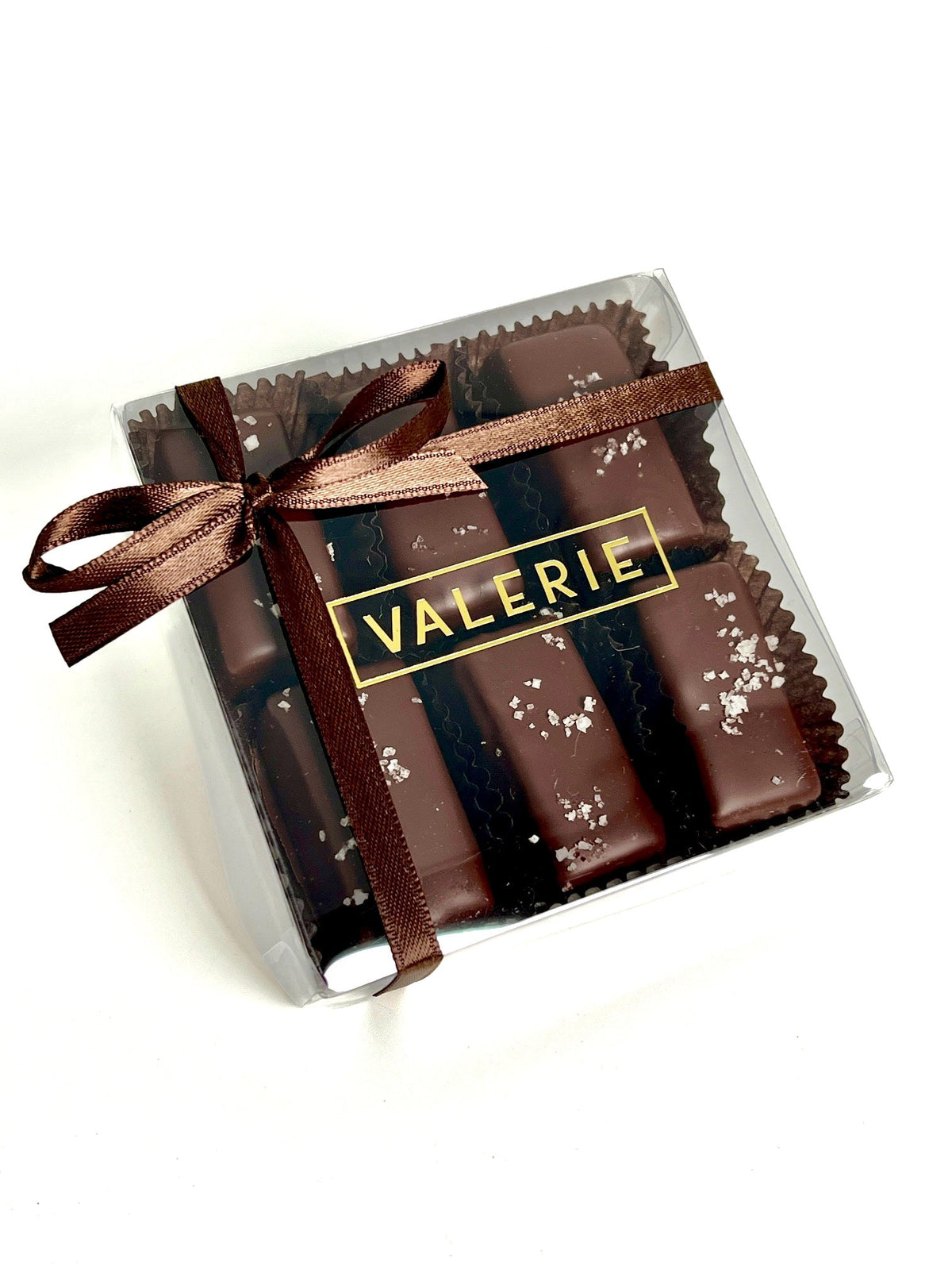 A beautifully packaged box of Fleur de Sel Caramels by Valerie Confections, wrapped in a brown satin ribbon, showcasing handcrafted chocolate-enrobed caramels finished with Fleur de Sel.