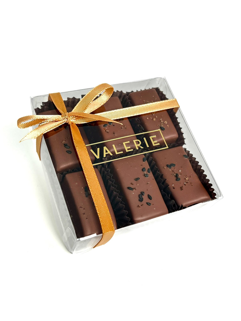 A beautifully packaged box of Rice & Sesame Caramels by Valerie Confections, wrapped in a golden satin ribbon, showcasing handcrafted chocolate-enrobed caramels finished with sesame and soy salt.