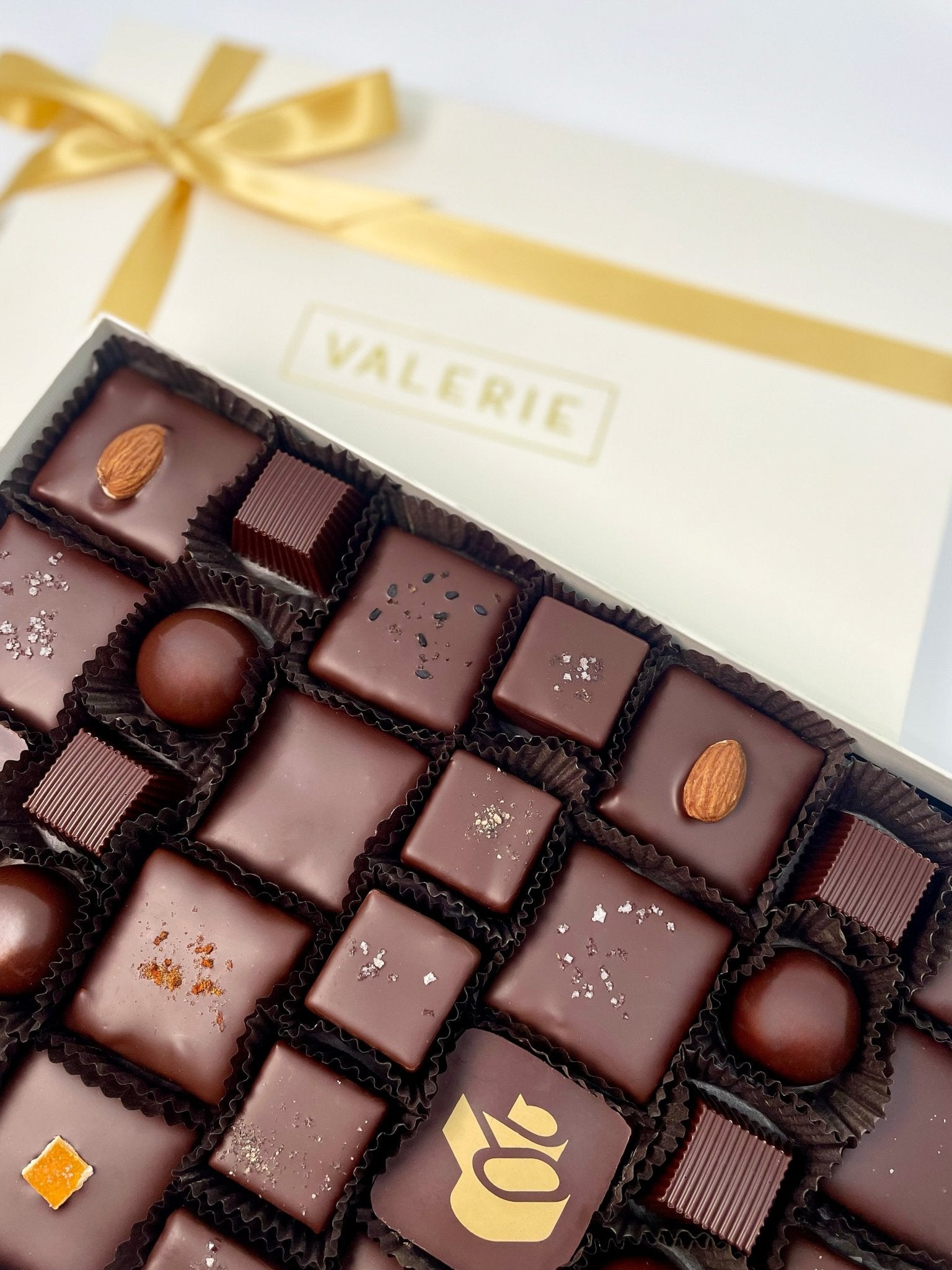 A luxurious Grand Assortment chocolate gift box with handcrafted toffees, truffles, and caramels, elegantly tied with a gold satin ribbon.