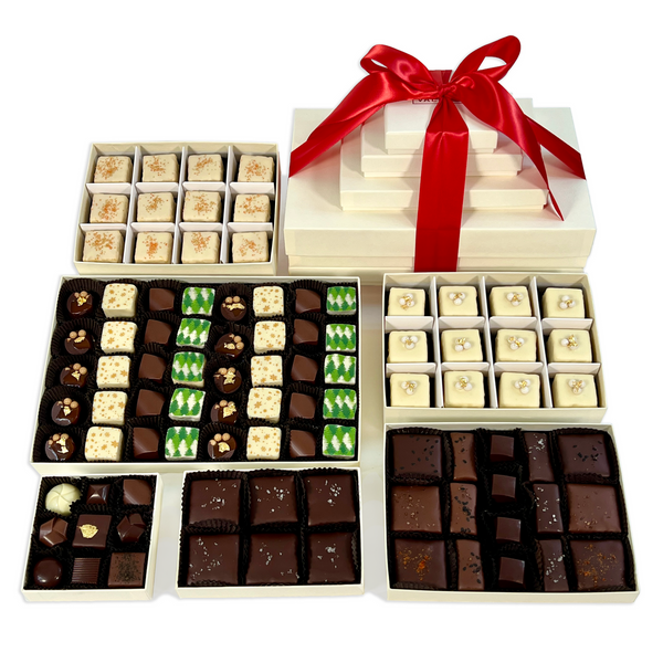 Valerie Confections Holiday Tower with stacked ivory boxes tied in red ribbon, filled with seasonal petits fours, truffles, toffees, and caramels.