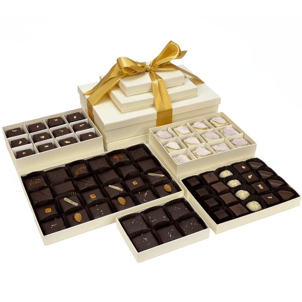 The Isabelle Gift Tower unwrapped, revealing an elegant assortment of chocolates, petits fours, and toffee in ivory boxes with a golden ribbon.