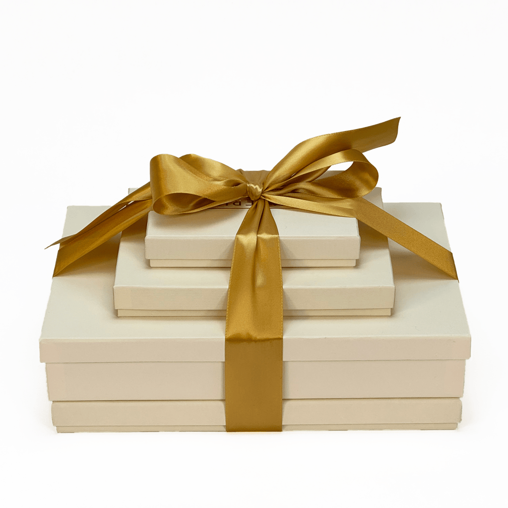 A beautifully wrapped Isabelle Gift Tower with stacked ivory gift boxes and a golden satin ribbon, perfect for luxurious gifting.