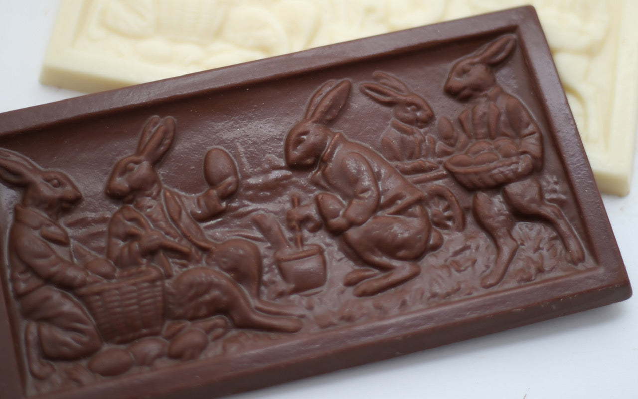 Close-up of a chocolate bar with a carved scene of four rabbits engaged in Easter activities.
