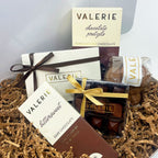 A collection of premium chocolates and confectioneries from Valerie, including a bittersweet chocolate bar, chocolate pretzels, cookies, and assorted chocolates, displayed on shredded paper packaging.