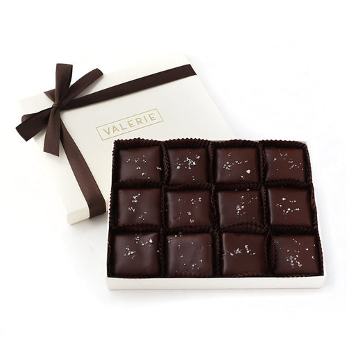 A luxurious 12-piece box of Almond Fleur de Sel Toffee dipped in rich bittersweet chocolate, elegantly presented in an ivory gift box with a brown satin ribbon.