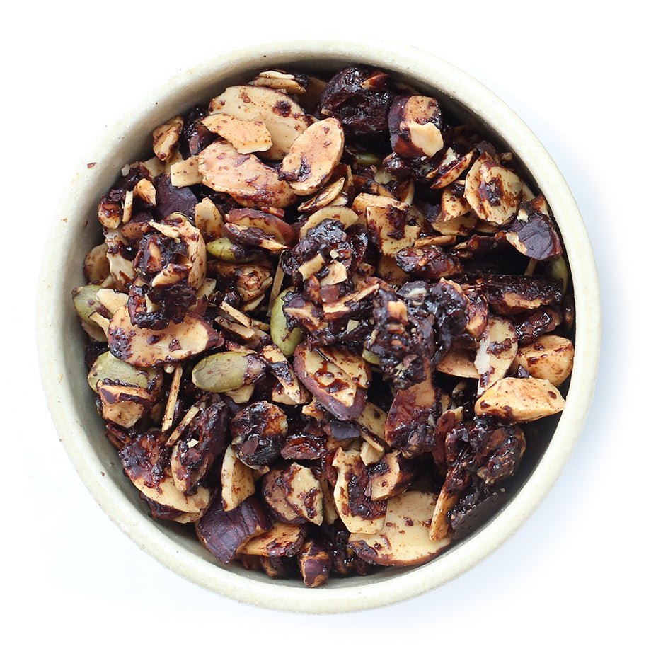 A bowl filled with rich chocolate granola, featuring almonds, hazelnuts, pepitas, cocoa nibs, and fleur de sel.