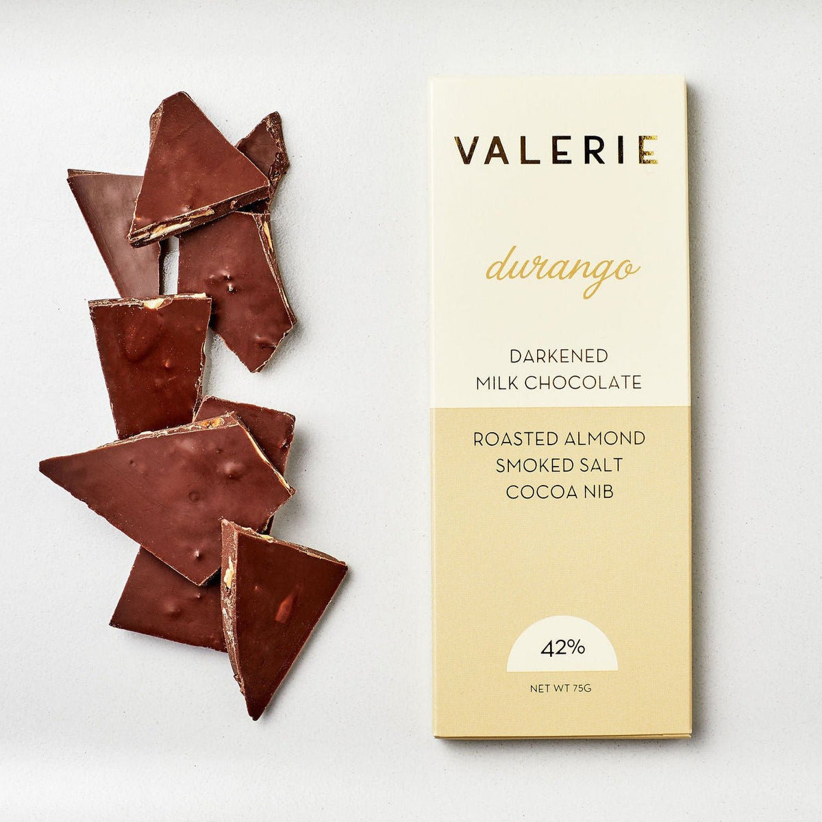 A Durango Bar made of darkened milk chocolate, roasted almonds, cocoa nibs, and hickory smoked salt, shown with broken chocolate pieces beside the packaging.
