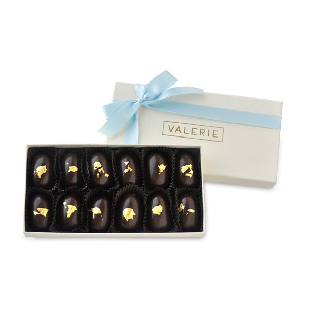 A luxurious box of 12 golden eggs, featuring dark chocolate caramel-filled eggs adorned with 23k gold leaf, tied with a light blue ribbon.