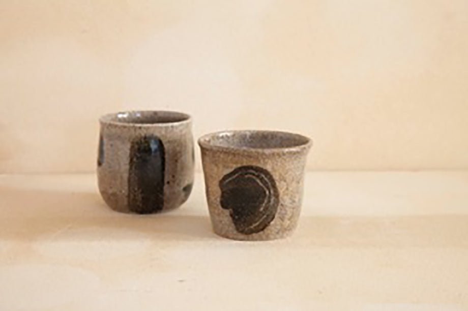 Two handmade tea cups with earthy textures and bold black glaze detailing, designed for a rustic yet modern aesthetic.