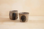 Two handmade tea cups with earthy textures and bold black glaze detailing, designed for a rustic yet modern aesthetic.