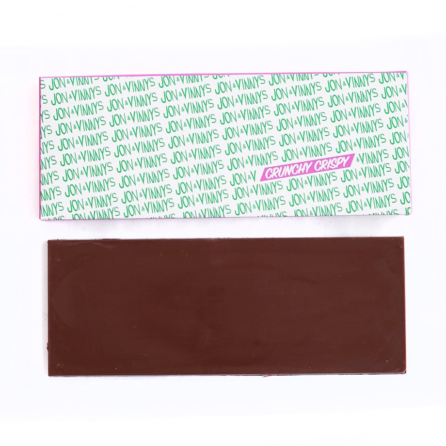 A Jon & Vinny's Crunchy Crispy Chocolate Bar, featuring a chocolate bar with crisp feuilletine layers, displayed alongside its branded packaging with green and pink text.