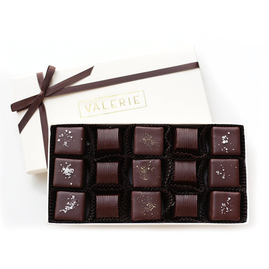 An elegant ivory gift box tied with a brown satin ribbon, filled with an assortment of Les Hommes Truffles, including Salt Truffles, Pepper Truffles, and Liquid Caramels enrobed in dark chocolate.