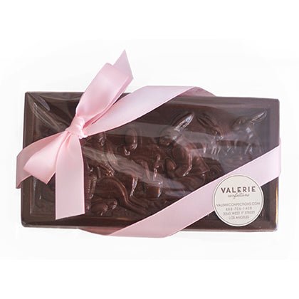 A handcrafted milk chocolate bar in elegant packaging, wrapped with a pink satin ribbon.