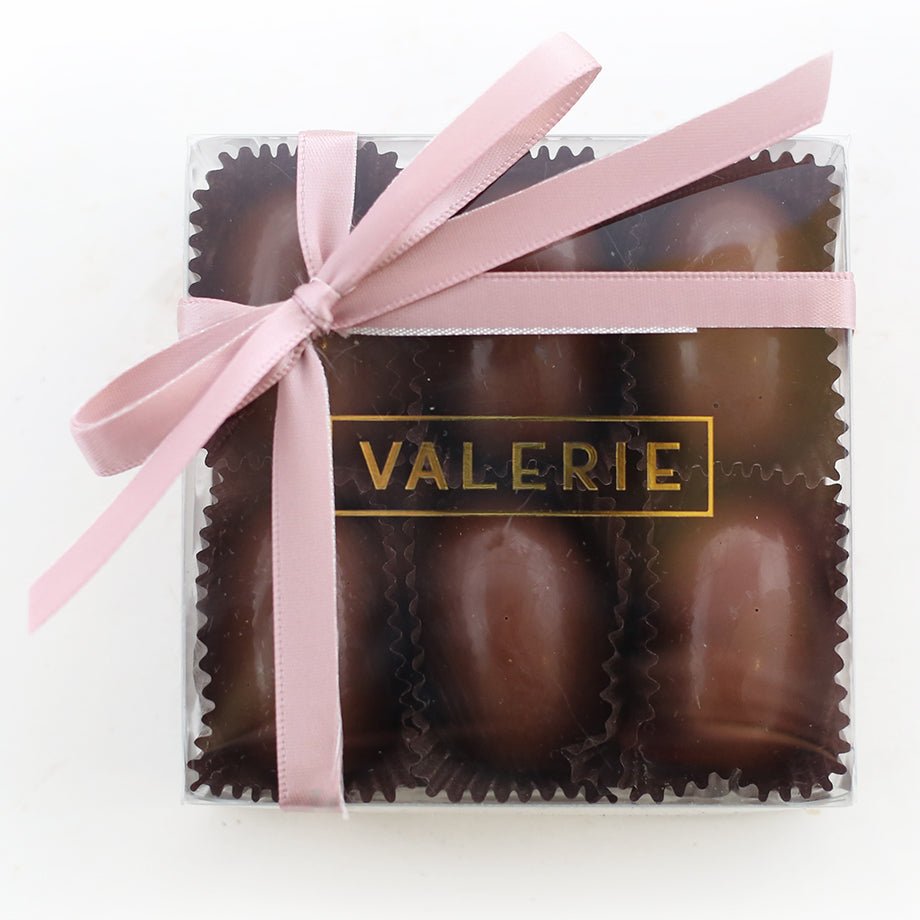 A set of smooth, milk chocolate ganache eggs, elegantly presented in a clear box with a pink ribbon.