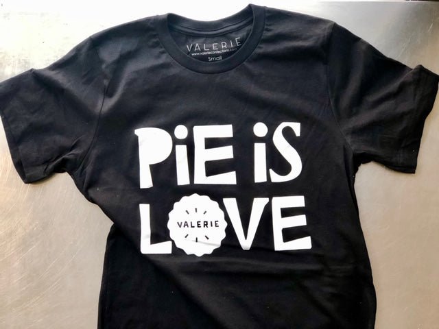 A black Pie Is Love t-shirt from Valerie Confections, featuring bold white lettering, a pie-shaped design element, and a relaxed fit. Designed by Eric Junker and printed in collaboration with Free & Easy.