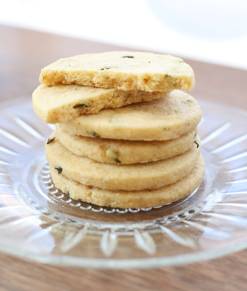 A stack of Valerie Confections’ Rosemary & Polenta Cookies on a glass plate, showcasing their golden crisp texture and flecks of fresh rosemary.