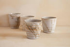 A collection of four handcrafted ceramic tea cups in neutral tones, featuring organic glazes and unique natural variations.