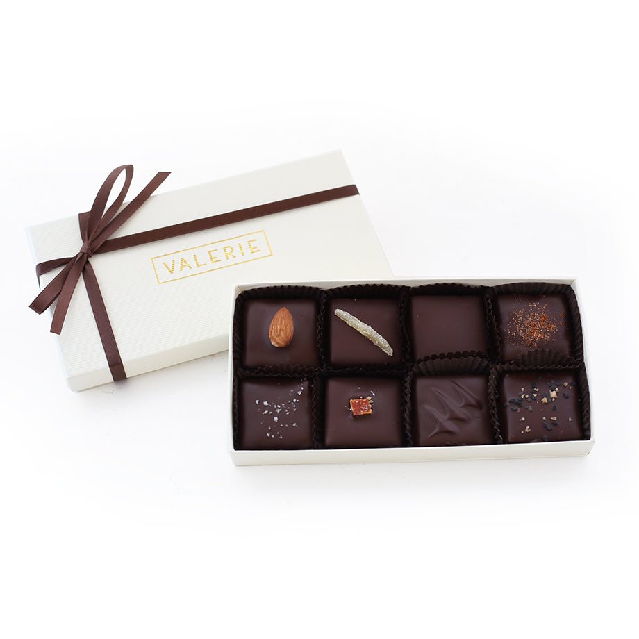Box of 8 assorted dark chocolates with various toppings and decorations. White box lid with &quot;VALERIE&quot; printed in gold and a dark brown ribbon bow.