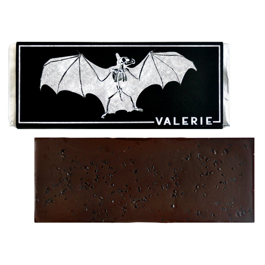 72% bittersweet chocolate bar sprinkled with black lava salt, shown both wrapped and unwrapped. The wrapper is metallic silver and black with a bat illustration and the name &quot;Valerie.&quot;