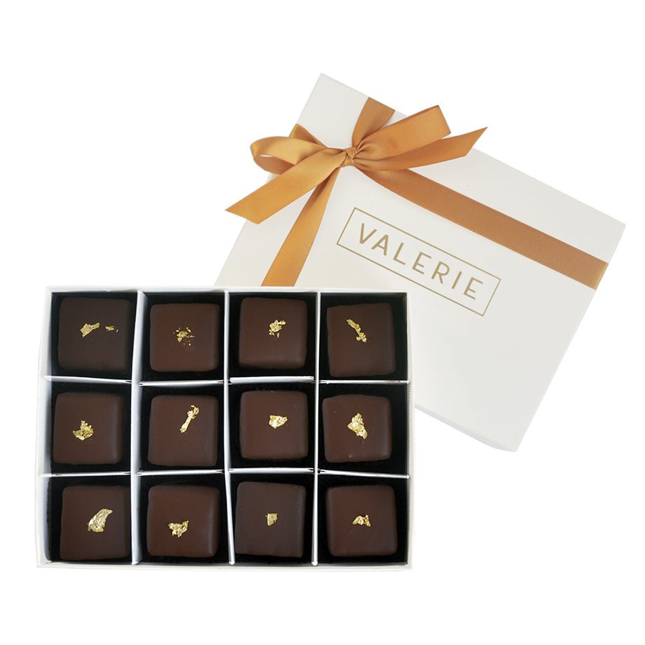 Box of twelve dark chocolate petits fours with gold leaf on top, in a white box with a gold ribbon and "VALERIE" written on the lid.