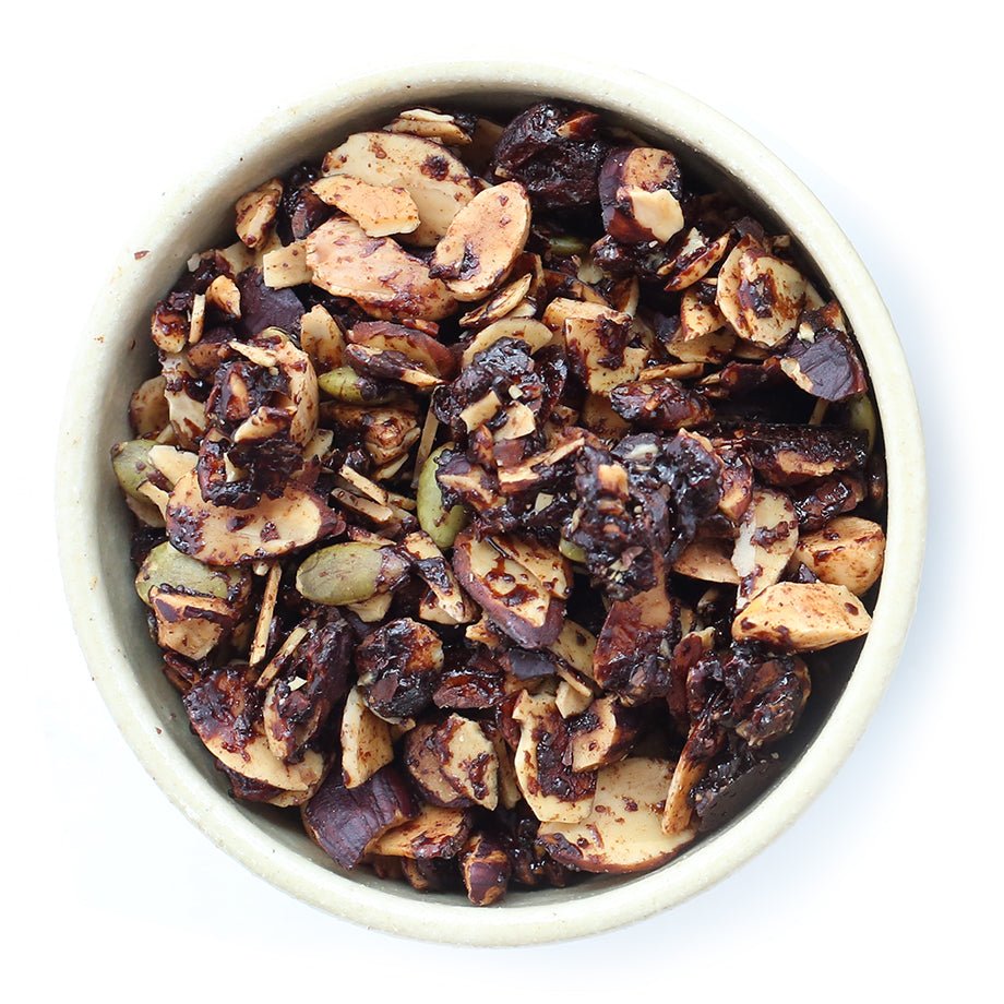 Bowl filled with granola containing almonds, cocoa nibs, hazelnuts, pepitas, and chocolate pieces.