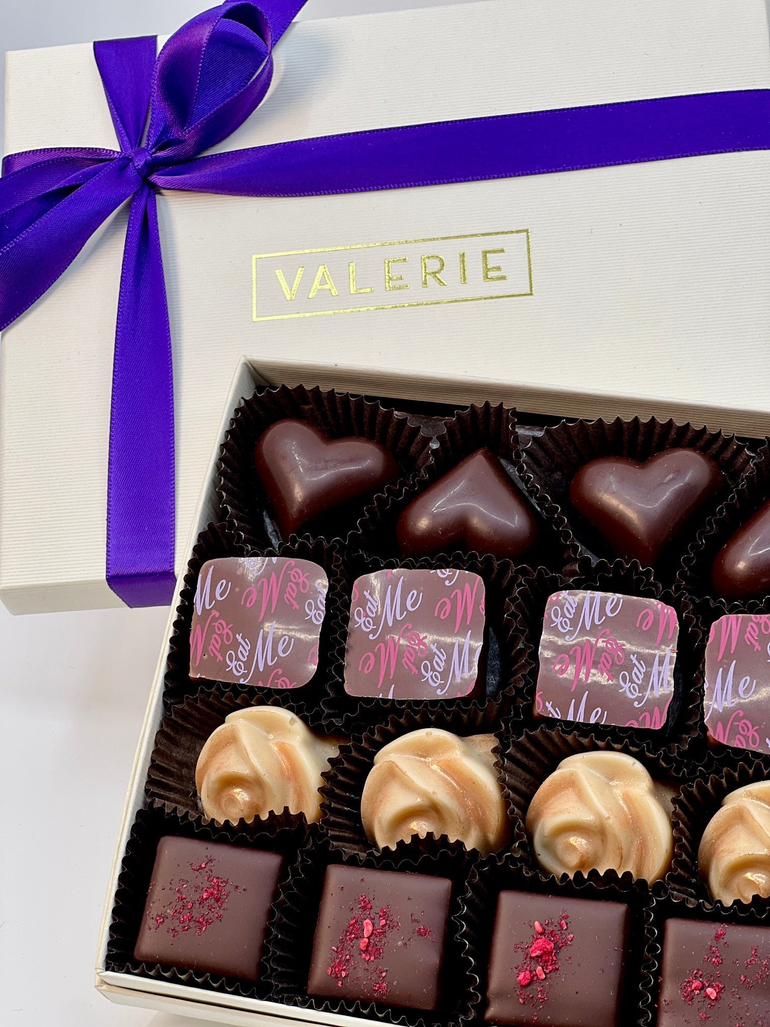 An open box of assorted chocolates tied with a purple ribbon.