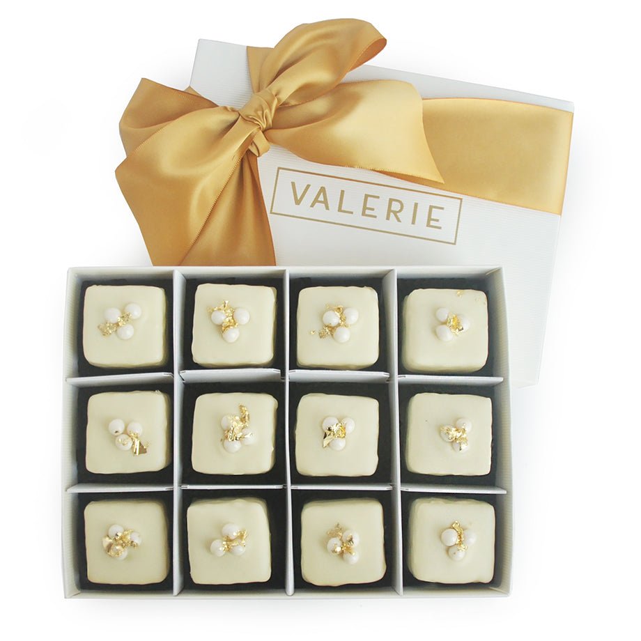 Box of 12 eggnog petits fours with white icing, decorated with white pearls and gold flakes, tied with a golden bow.