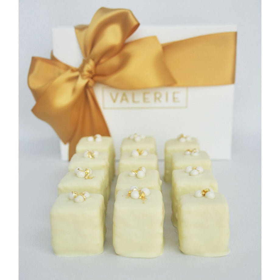 White box with golden bow and "Valerie" text, twelve white-chocolate petits fours with decorative toppings in front.