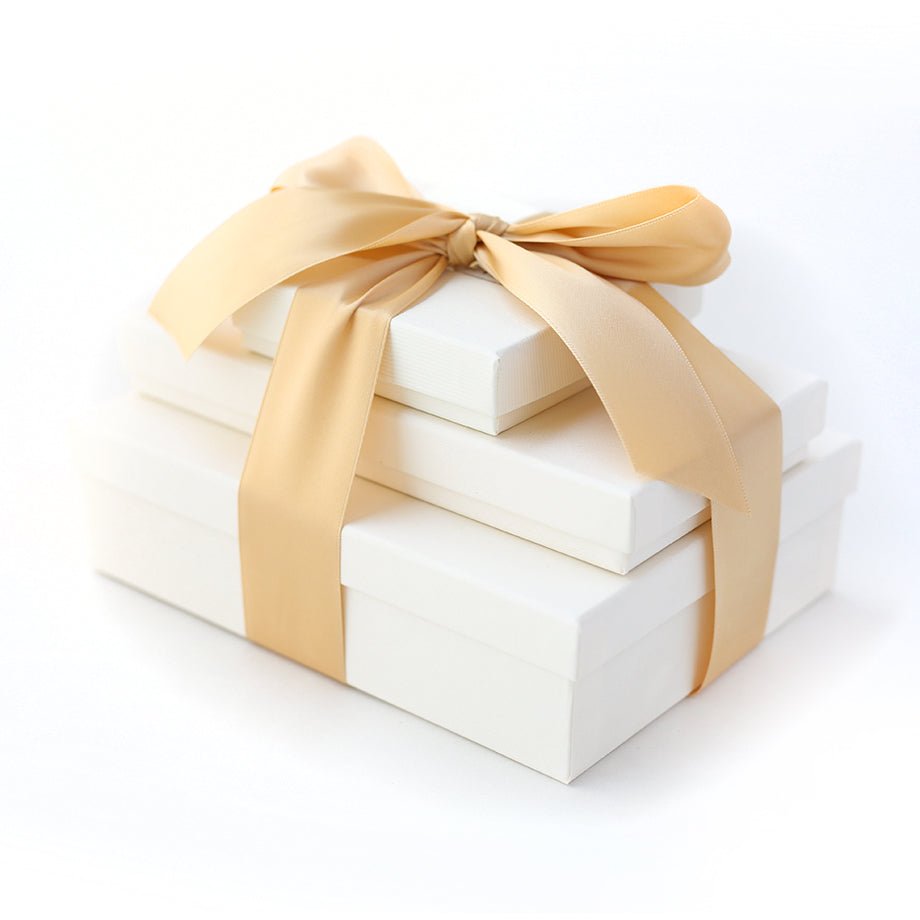 Stack of three white gift boxes tied with a gold satin ribbon bow.