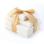 Stack of three white gift boxes tied with a gold satin ribbon bow.