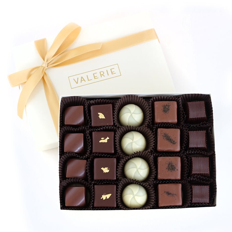 A beautifully arranged gourmet truffle assortment in a white gift box with a golden ribbon, featuring handcrafted chocolates with rich flavors.