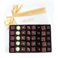 A beautifully presented large gourmet truffle assortment in an elegant ivory box with a golden ribbon, featuring handcrafted chocolate truffles in various flavors.
