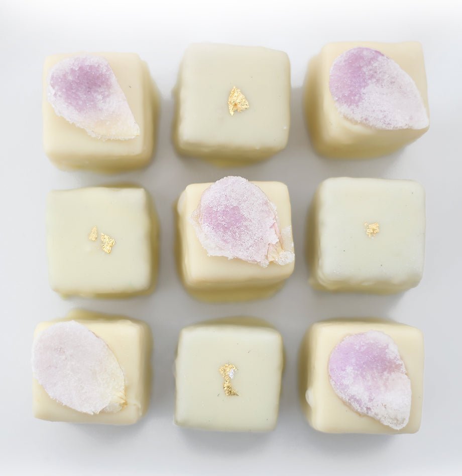 A close-up of Matcha and Rose Petal Petits Fours, delicately coated in white chocolate and adorned with gold leaf and candied rose petals.