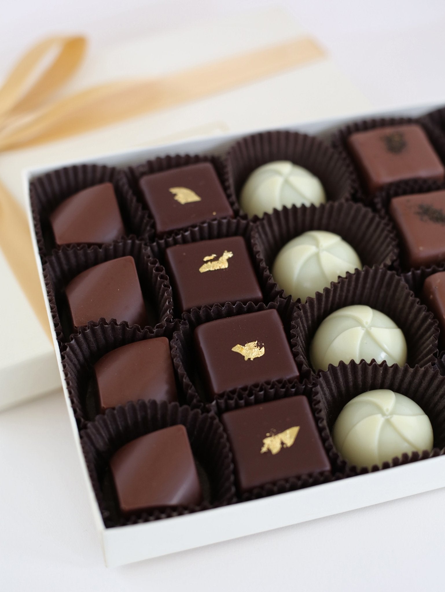 A close-up of a luxurious chocolate truffle assortment, highlighting gold leaf-adorned truffles, Matcha, Earl Grey, and Liquid Caramel chocolates.