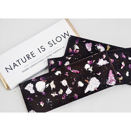 Chocolate bar adorned with candied and dried rose petals and its packaging that reads "NATURE IS SLOW".