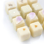 A close-up of assorted white chocolate petits fours, featuring Rose Petal, Lavender, Earl Grey, and Lemon flavors, elegantly decorated with candied flowers.
