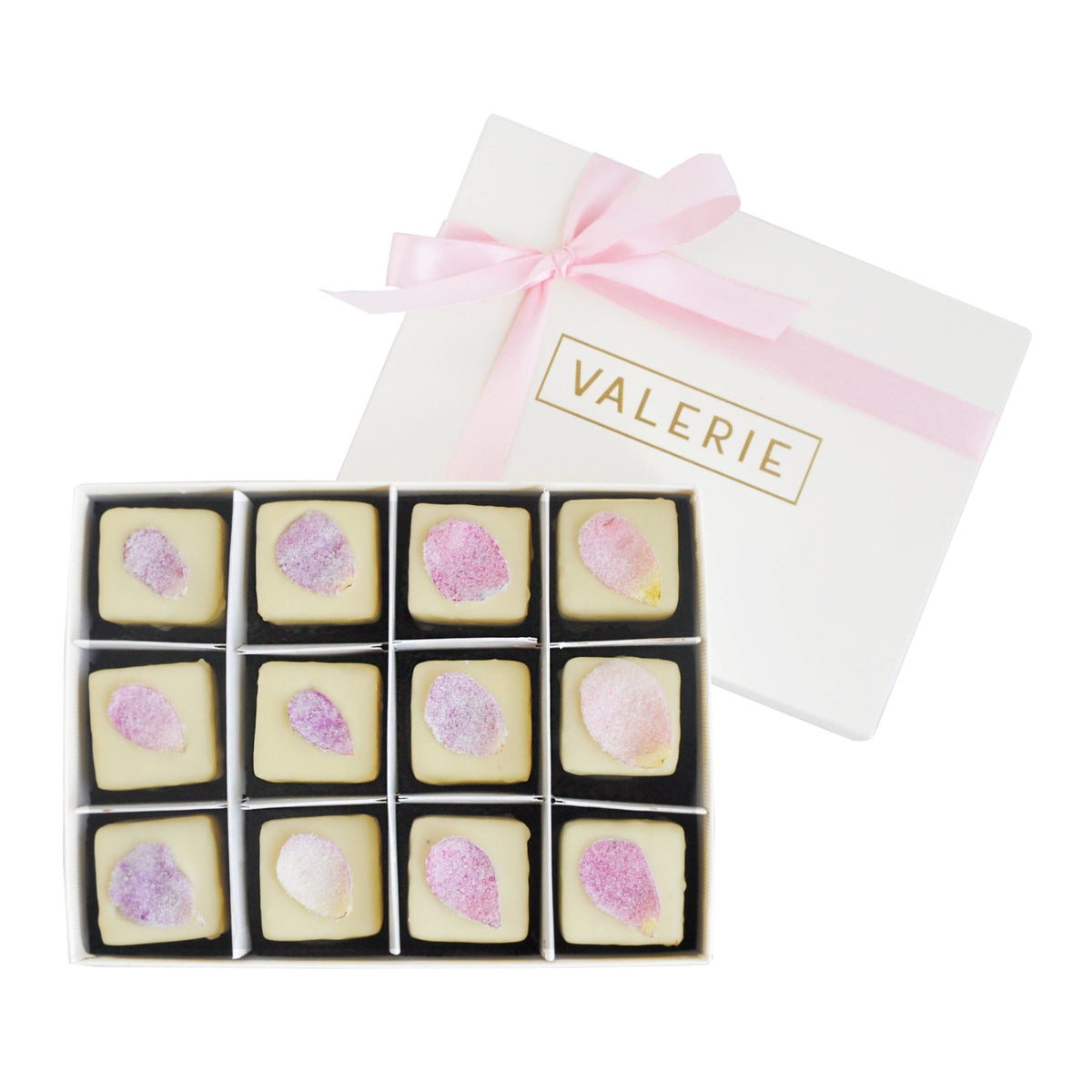 Open box of 12 white chocolate petits fours topped with candied rose petals in shades of pink and purple.