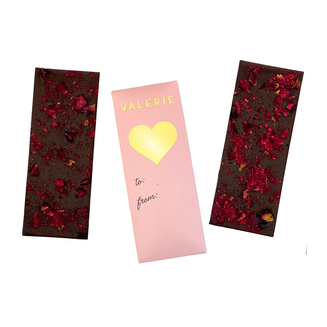 Two chocolate bars with red rose petals and raspberries beside a pink wrapper with "VALERIE" and a gold heart.