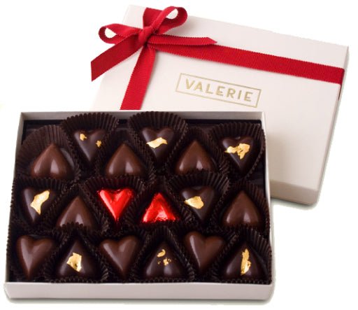 Box of heart-shaped chocolates, mostly bittersweet with three wrapped in red foil and some decorated with gold leaf.