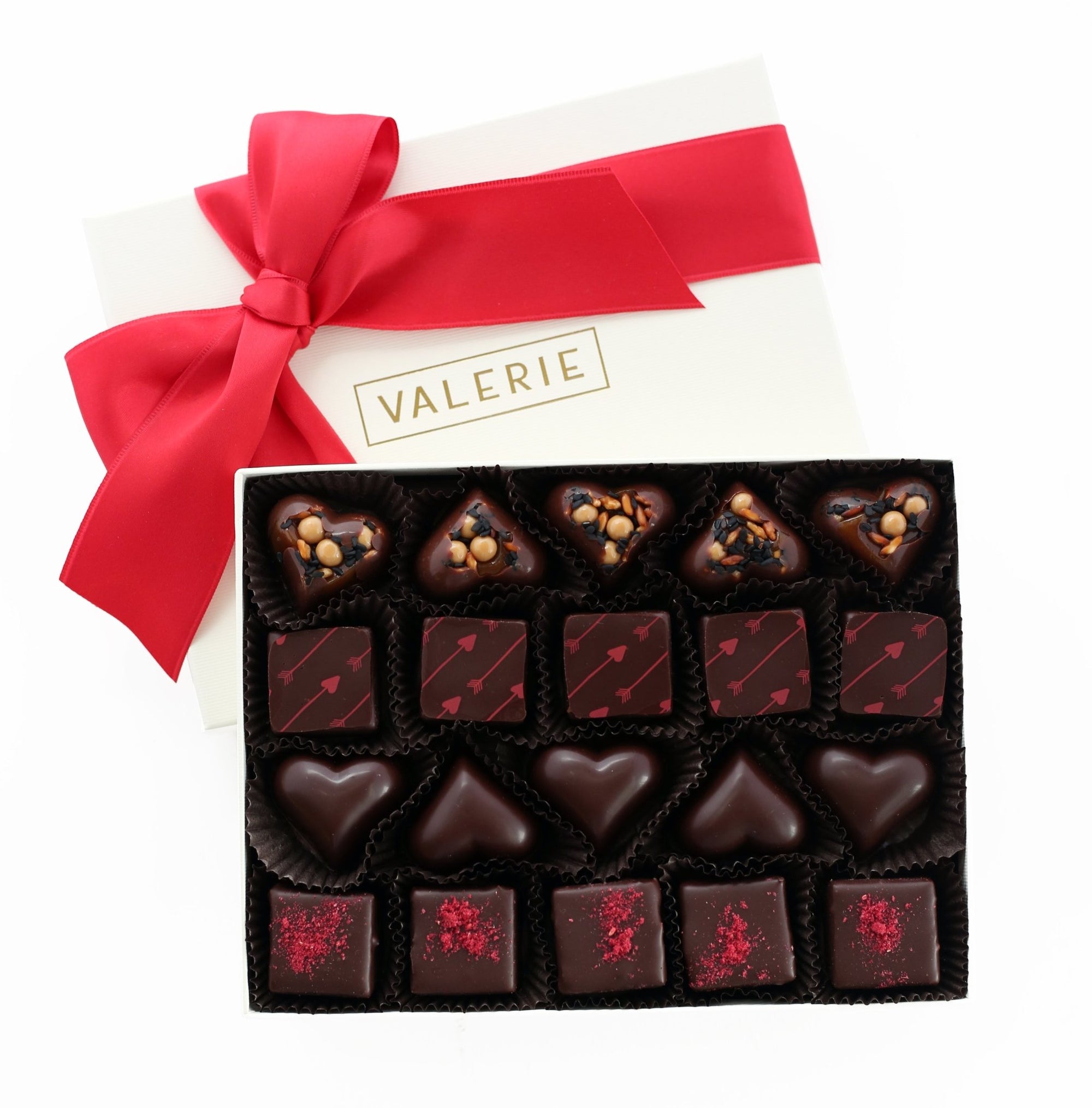 Open box of assorted chocolates with various shapes and decorations, on a white surface with a red ribbon.