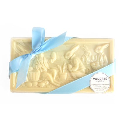 Rectangular white chocolate bar with Easter rabbit design, wrapped in clear plastic with a light blue ribbon bow and a white Valerie sticker.